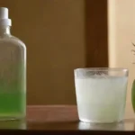 Botella de gel de aloe vera junto a un vaso de agua y un cepillo dental.
