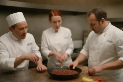Chefs en una cocina vibrante compartiendo historias mientras condimentan platos con pimienta negra.
