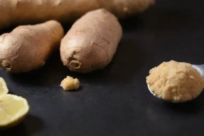 Cerrar las raíces frescas de jengibre y una cuchara de medición junto a un guía de salud.