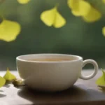 Hojas de Ginkgo y suplementos mostrados con una taza de té en un entorno natural.