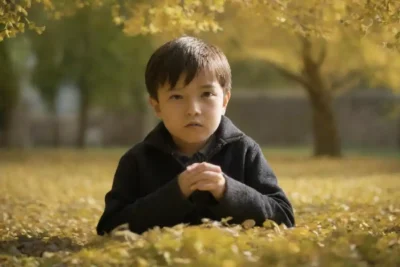 Un niño pequeño junto a hojas de ginkgo biloba en un entorno natural.