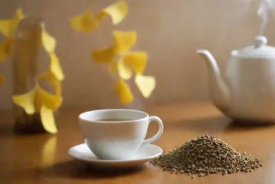 Hojas de ginkgo seco y semillas dispuestas junto a una taza de té de ginkgo.