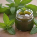 Un frasco de ungüento casero colocado junto a hojas de menta frescas y un masaje relajante.
