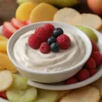 Un cuenco de turba cremosa rodeado de rodajas de fruta fresca y galletas.