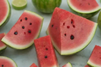 Una rodaja de sandía vibrante rodeada de productos de cuidado de la piel y frutas frescas.