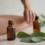 Hojas de eucalipto y botella de aceite esencial junto a una persona frotando sus músculos doloridos.