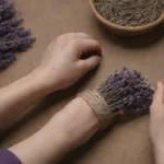 Manos fabricando un collar lavanda con flores secas y gemelas.