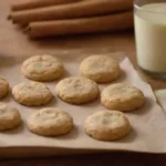 Una bandeja de galletas de canela recién horneadas junto con un libro de recetas e ingredientes.