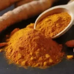 Una cucharada de polvo de cúrcuma junto a raíces de cúrcuma frescas