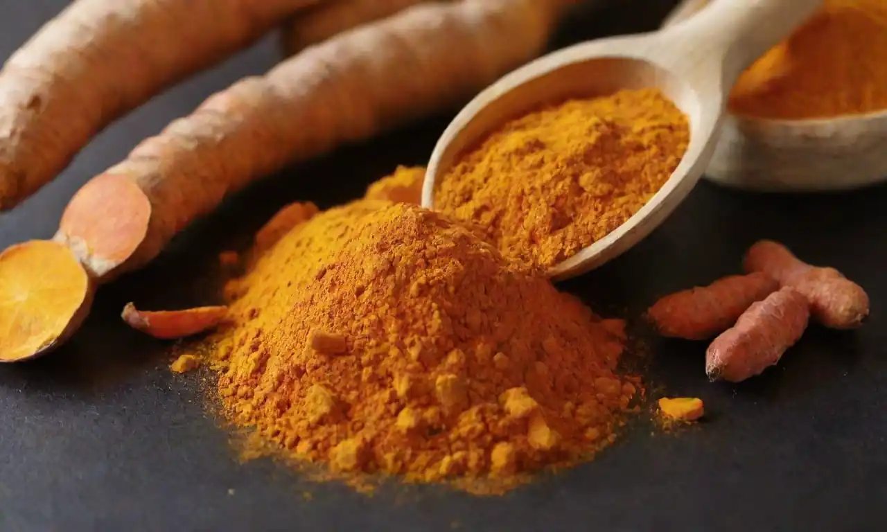 Una cucharada de polvo de cúrcuma junto a raíces de cúrcuma frescas