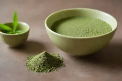 Un tazón de matcha en polvo junto a hojas de té verdes