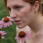 Un acercamiento de una persona con una erupción rodeada de flores de echinacea.